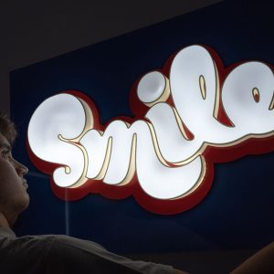 Néon LED Smile com letras 3D brancas e contorno vermelho sobre acrílico azul – Kami Studio